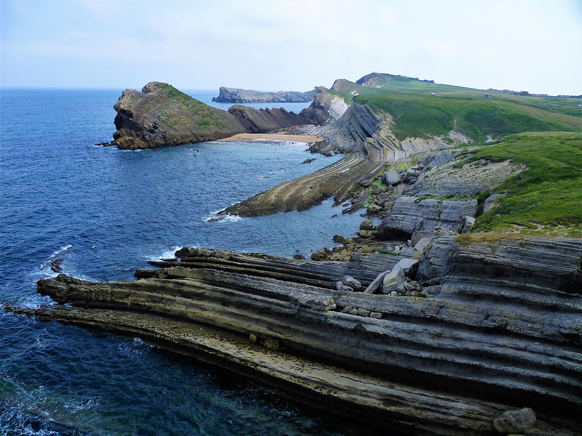 A scenic view of a rocky coastline with cliffs extending into the ocean. The landscape is lush and green, with waves crashing against the rocky shore.
