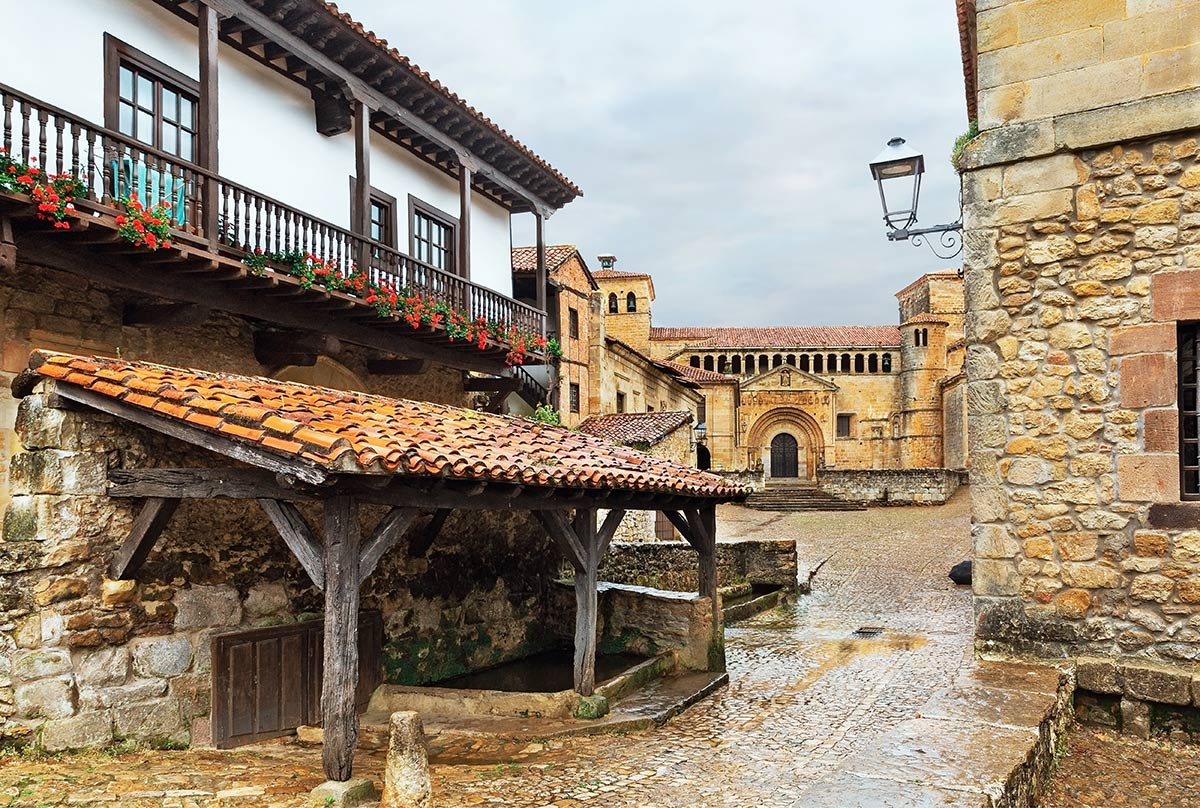 Historic stone buildings with a traditional wooden structure and a tiled roof, surrounded by a cobblestone street and an old church in the background.