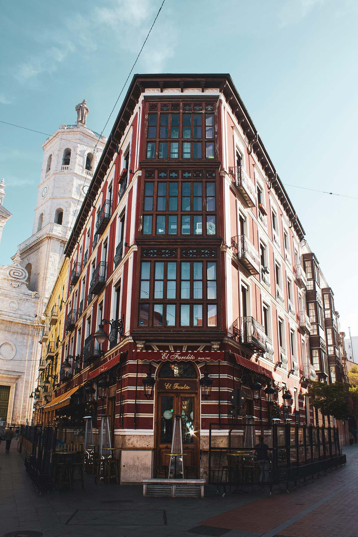 View of a historic building in the city, featuring a red facade with large windows, balconies, and the 'El Favorito' restaurant at the base, located near a church tower.