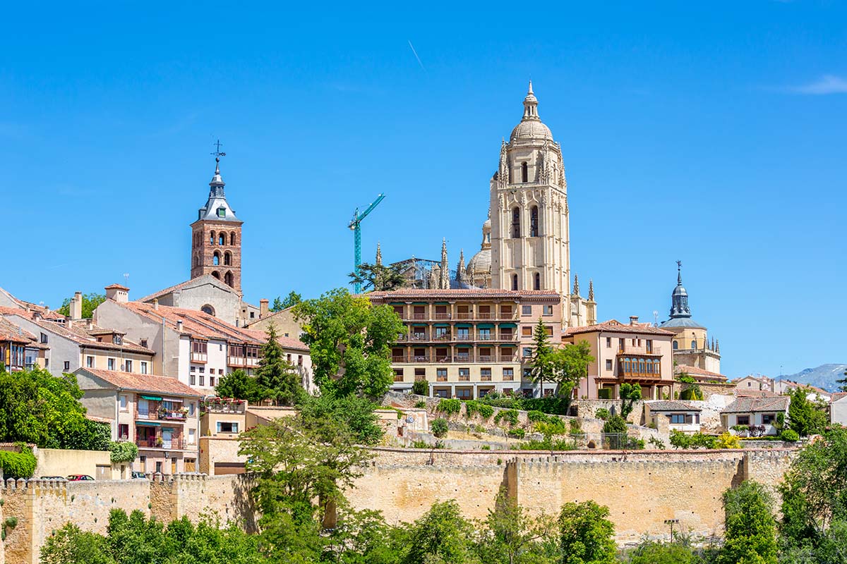 Panoramic view of a town with a prominent church tower, residential buildings, and a construction crane in the background, all under a bright blue sky.