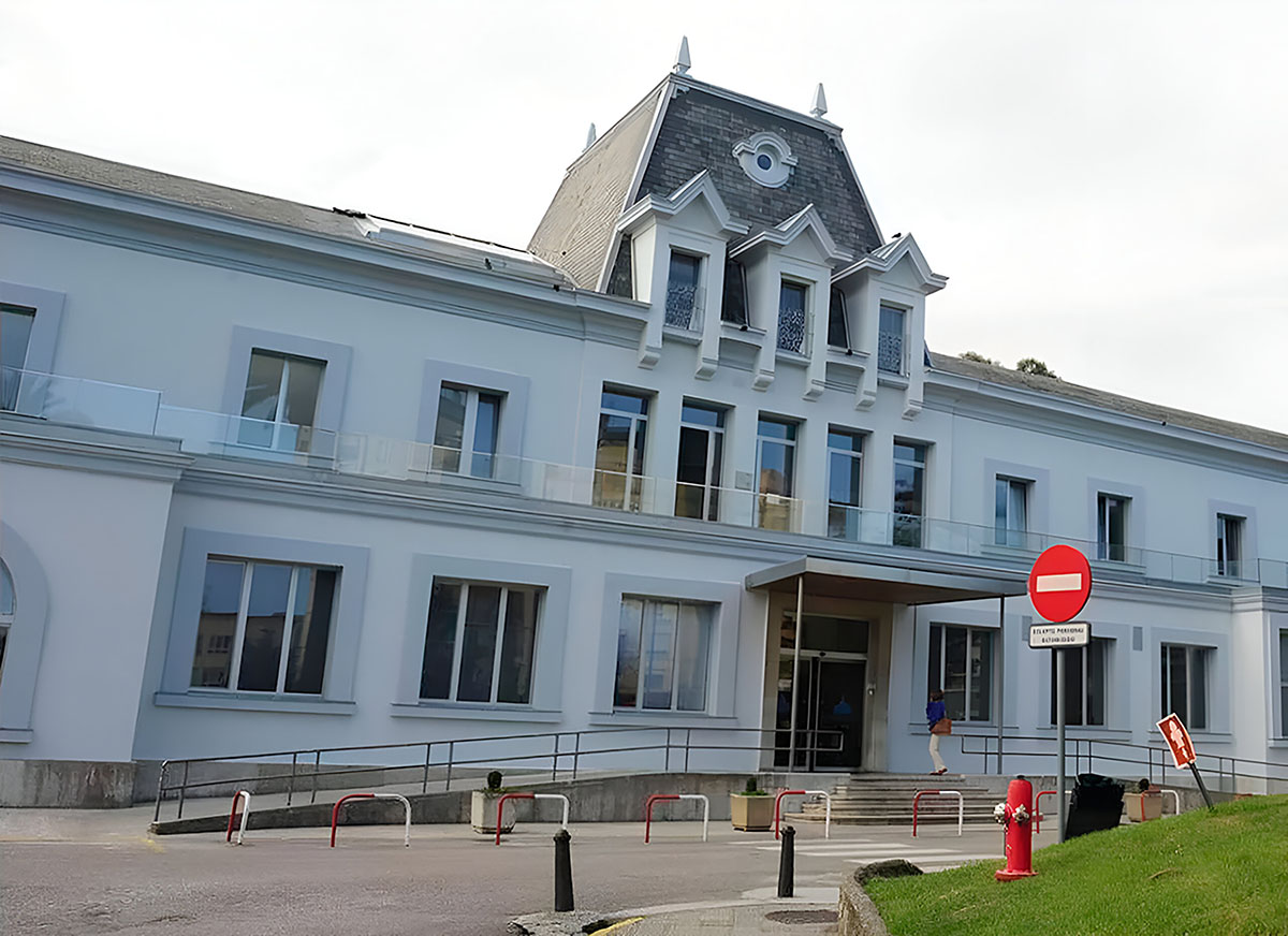 Exterior view of a modern building with a distinctive architectural style, featuring a ramp entrance, no-entry sign, and a fire hydrant in front.